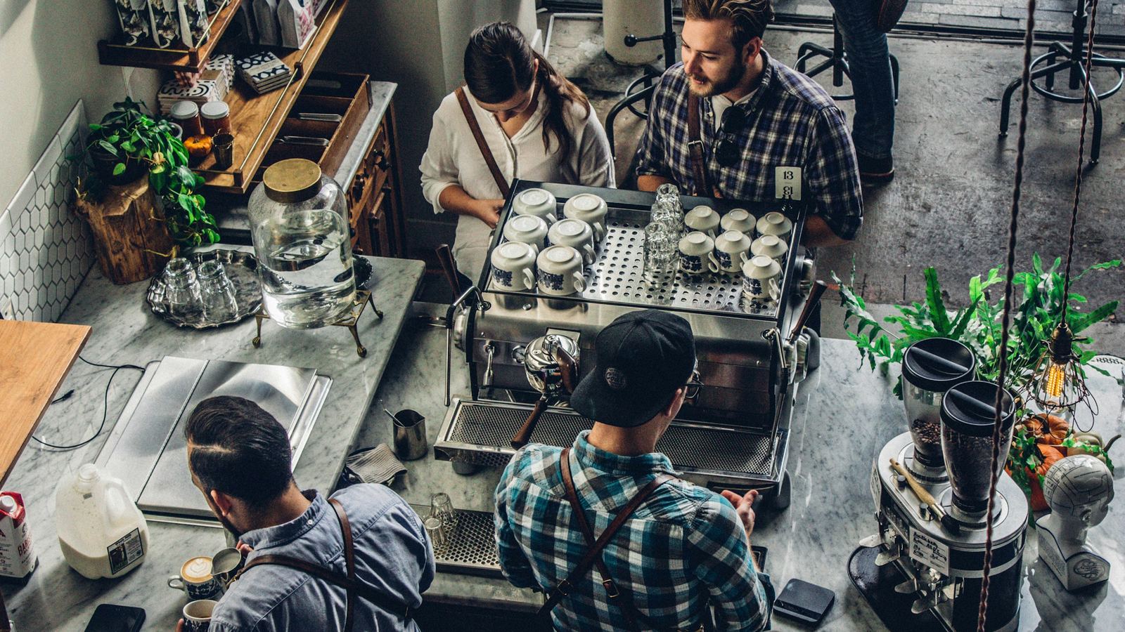 Baristas working at an espresso machine behind a coffee bar, seen from above