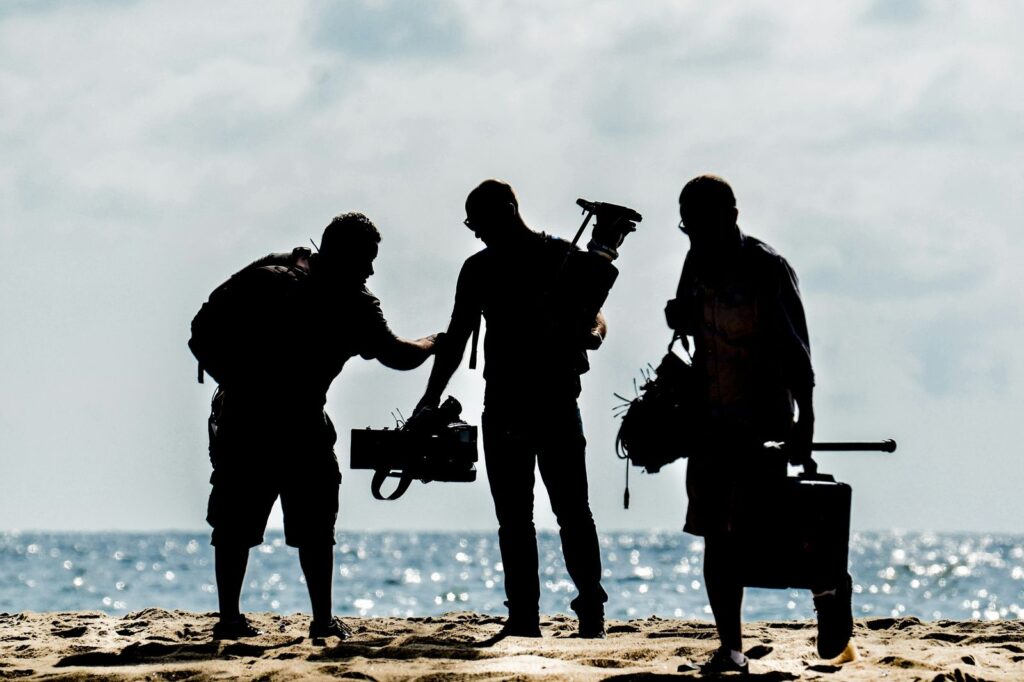 Silhouette of a film crew carrying a camera and equipment on a beach